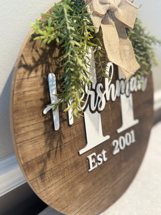 Wooden sign with 'Hersham' and 'Est 2001' text, decorated with greenery and a bow.