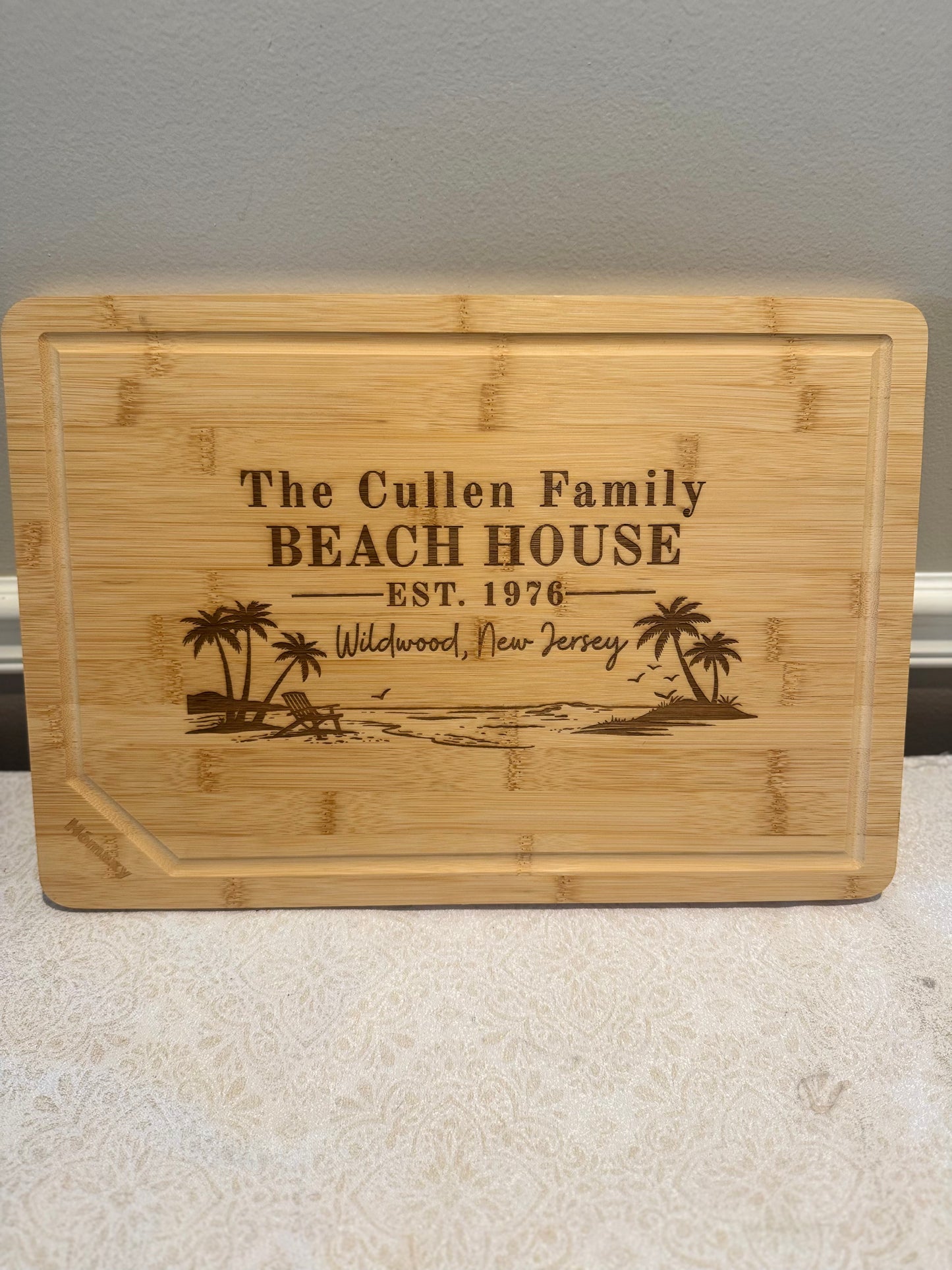 Bamboo cutting board with engraved text and beach scene design on a neutral background