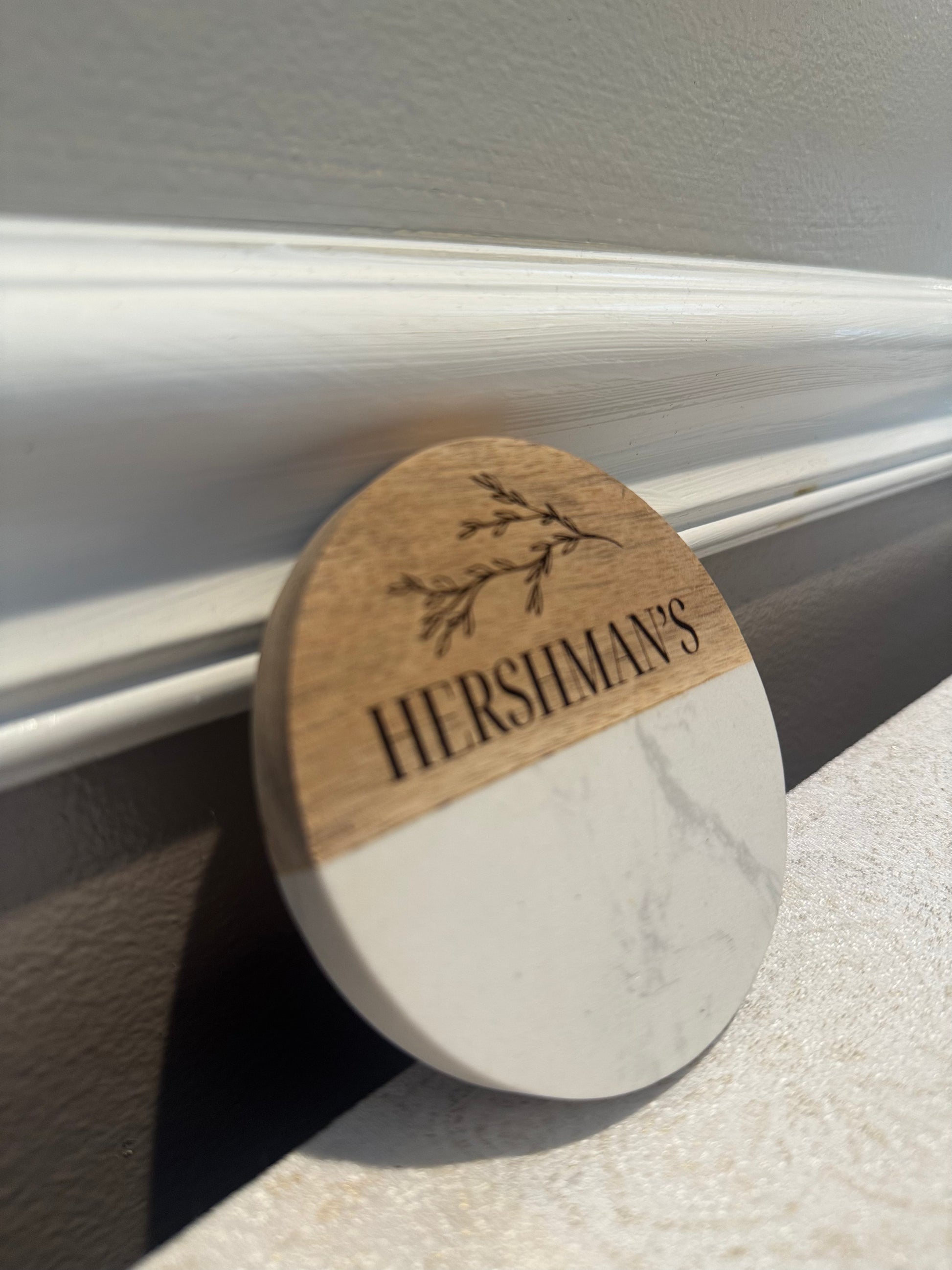 Round marble coaster with wooden accent and 'Hershiman's' engraving on a gray surface.