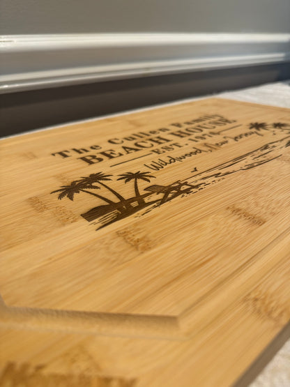 Wooden cutting board with engraved text and palm tree design on a white surface.