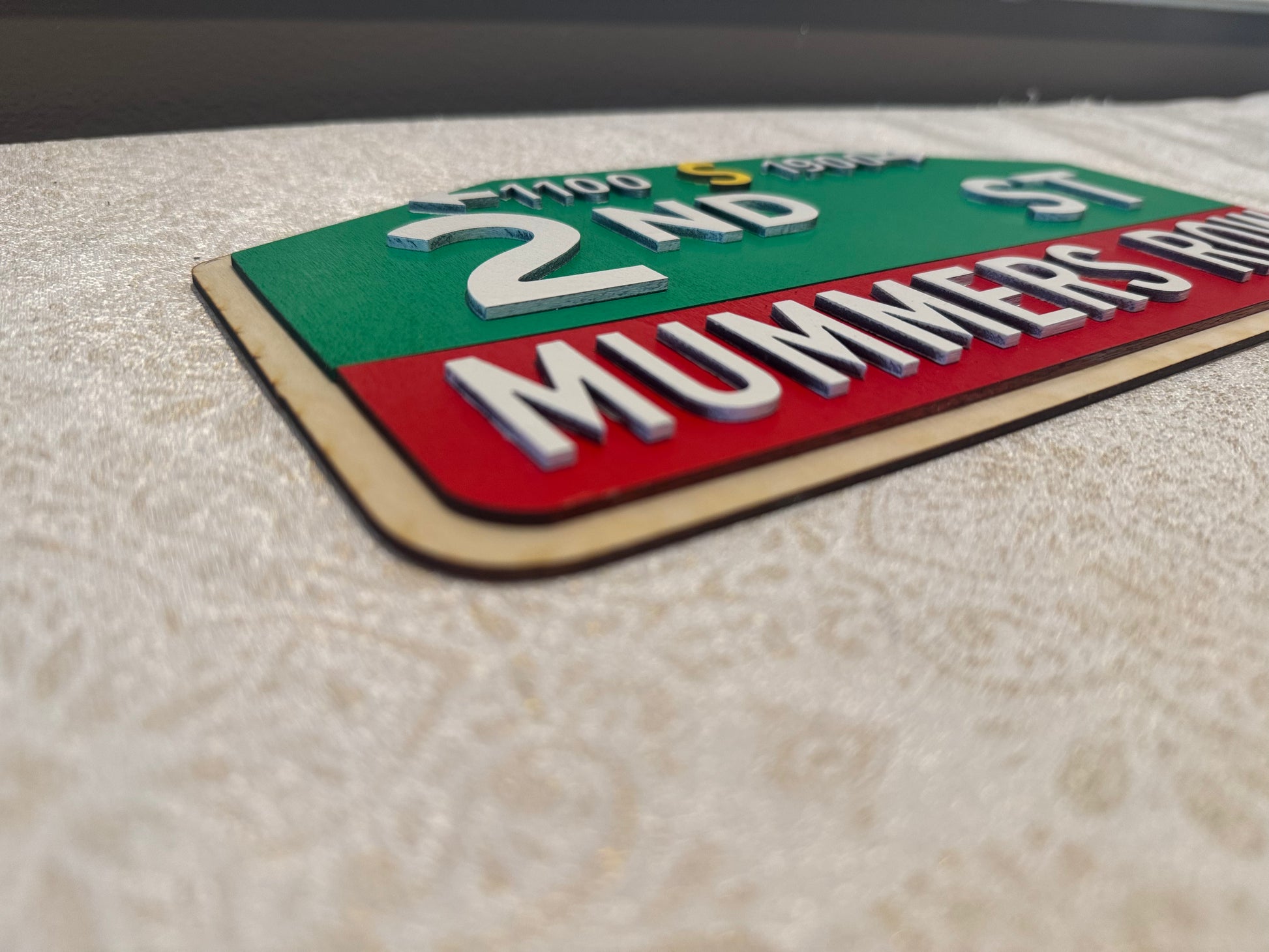 Street sign for '2nd St MUMMERS ROW' on a textured surface