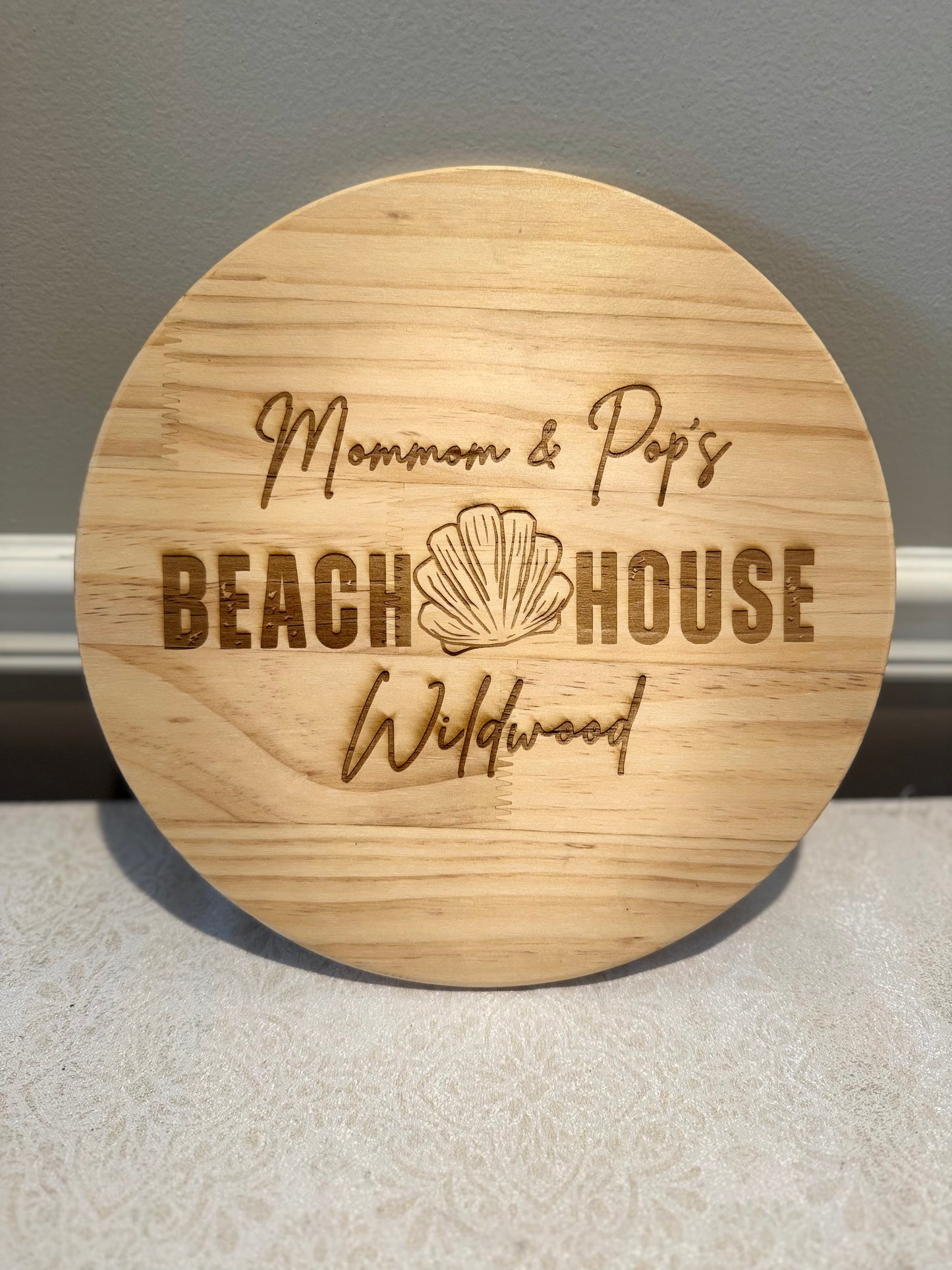 Round wooden sign with engraved text and shell design on a neutral background