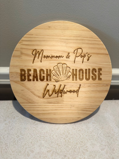 Round wooden sign with engraved text and shell design on a neutral background