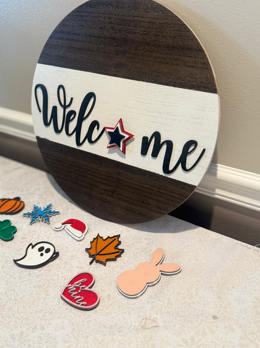 Round wooden sign with 'Welcome' text and decorative pins on a surface.