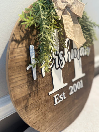 Wooden sign with 'Hersham' and 'Est 2001' text, decorated with greenery and a bow.