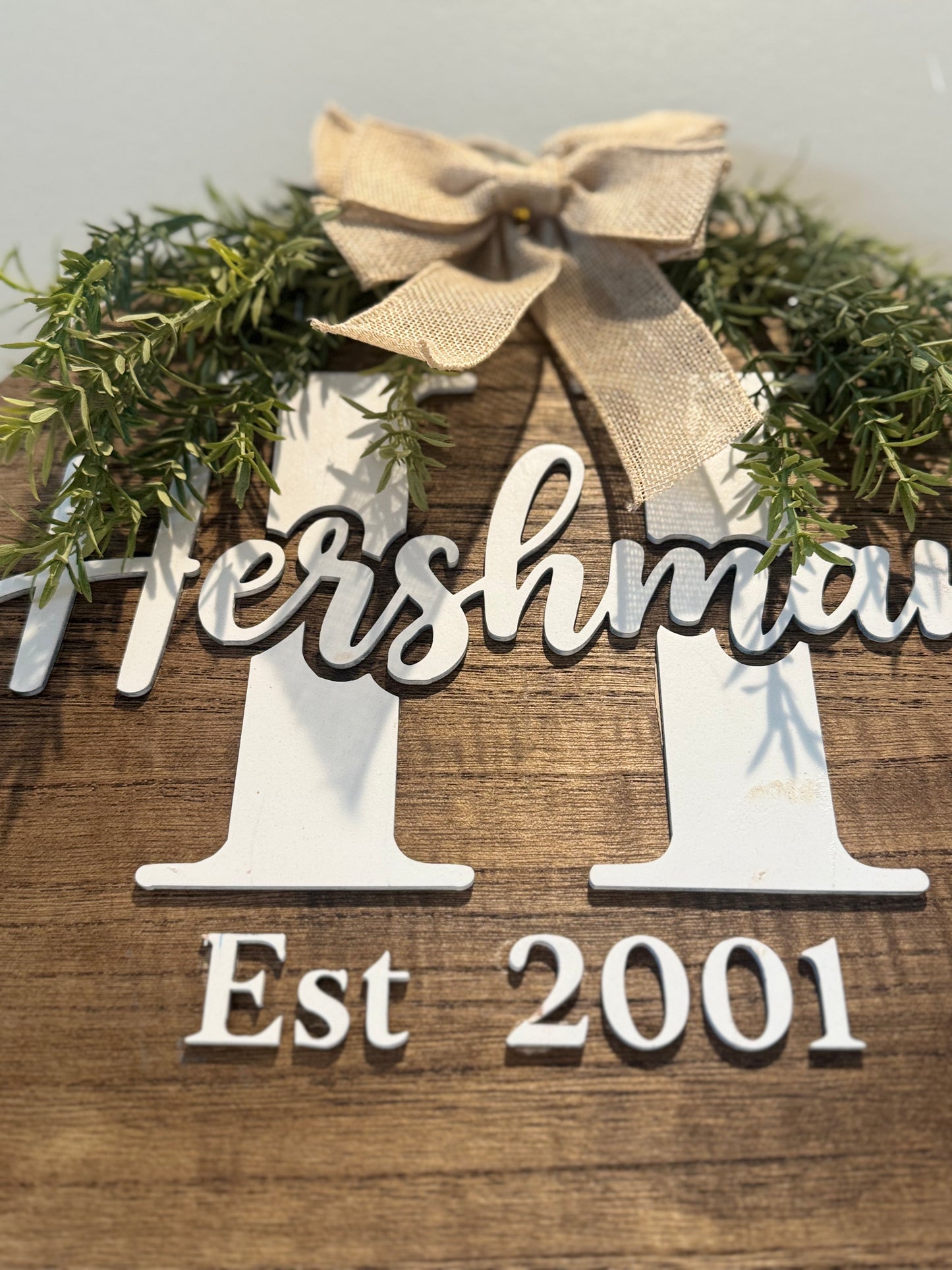 Wooden sign with 'Hersham' and 'Est 2001' text, decorated with a bow and greenery.