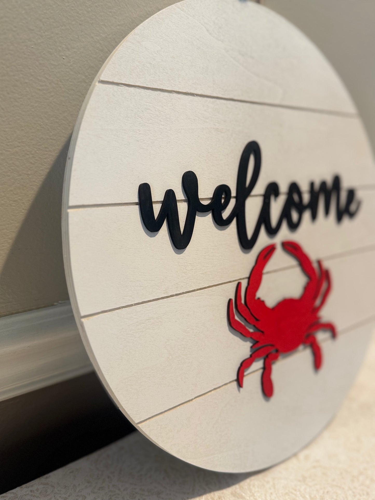 Round wooden sign with 'Welcome' text and red crab design on a neutral background