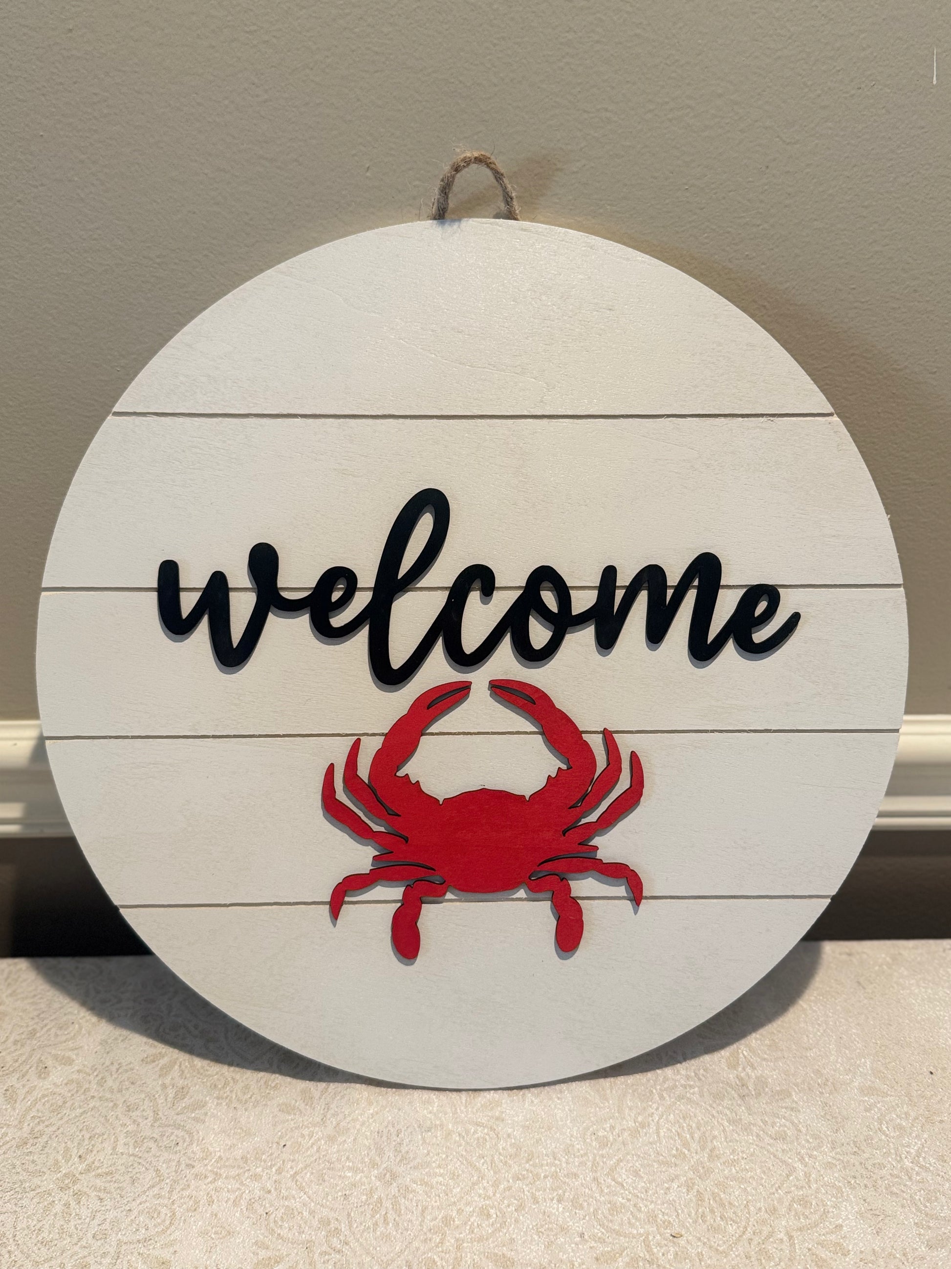 Round wooden sign with 'welcome' text and red crab design on a neutral background