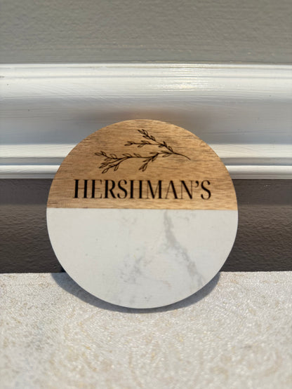 Round marble coaster with wooden top and 'HERSHMAN'S' branding on a neutral background