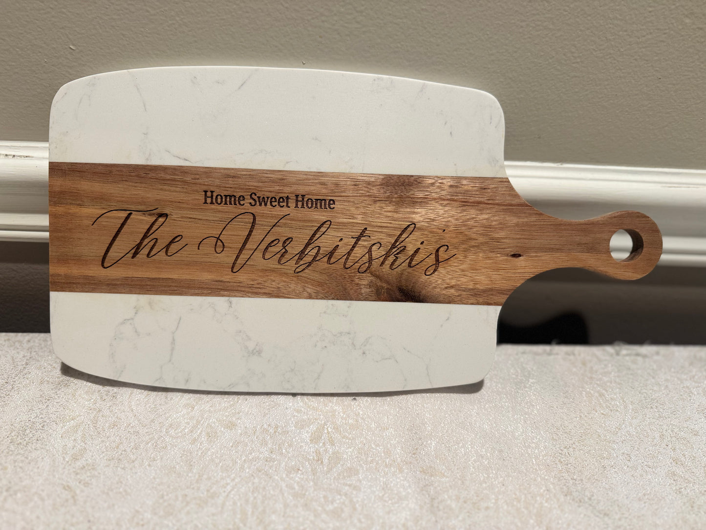 Marble cutting board with wooden handle and engraved text on a neutral background