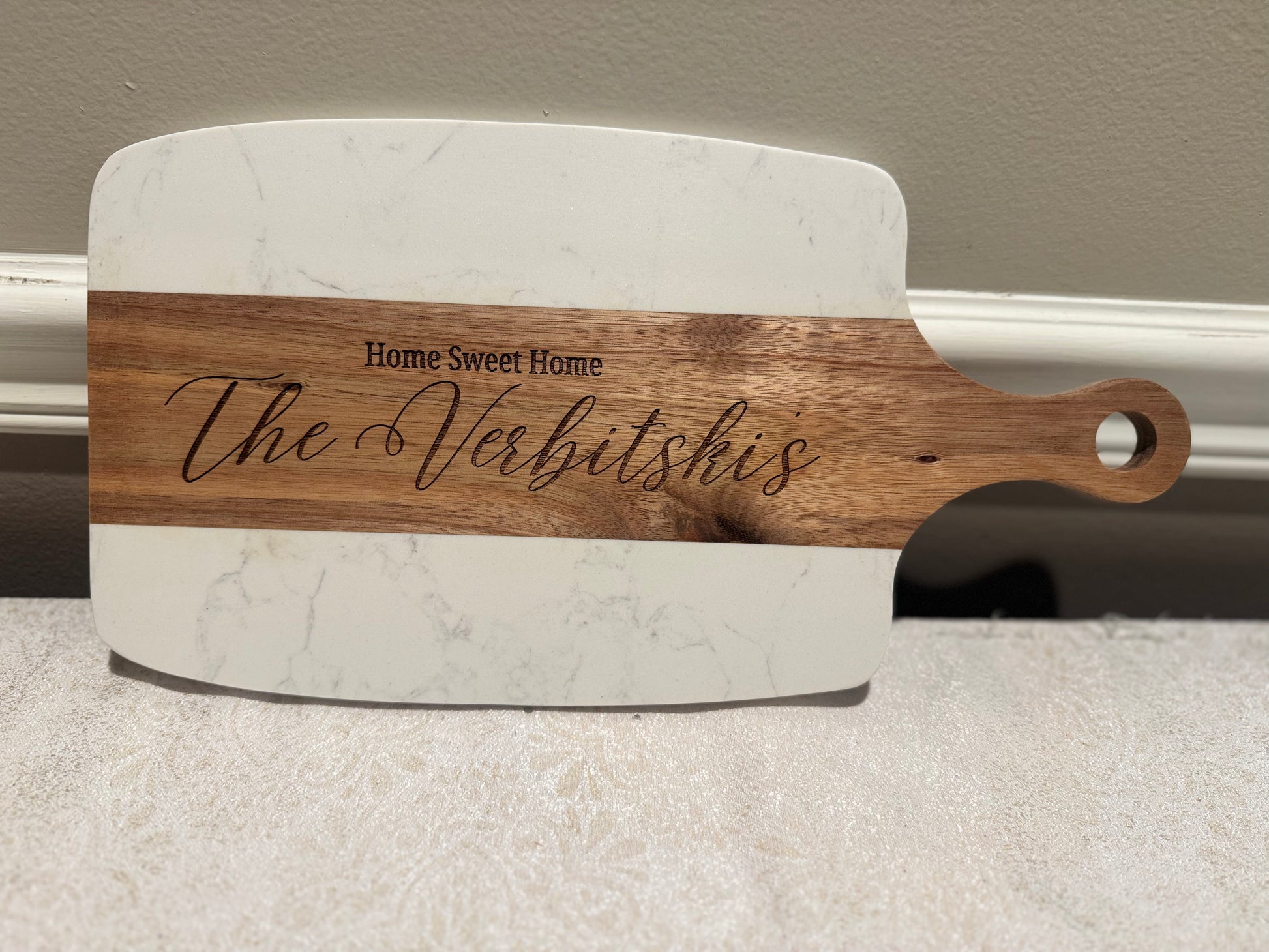 Marble cutting board with wooden handle and engraved text on a neutral background