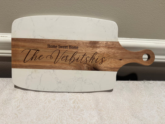 Marble cutting board with wooden handle and engraved text on a neutral background